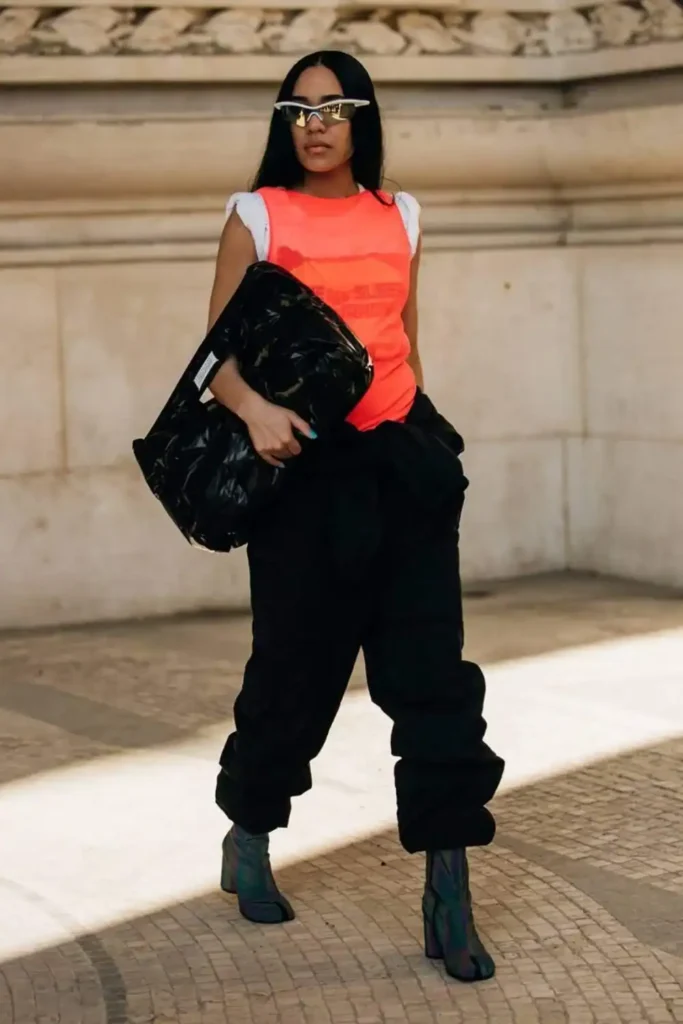 trendy woman wearing orange top, black cargo trousers and black tabi boots