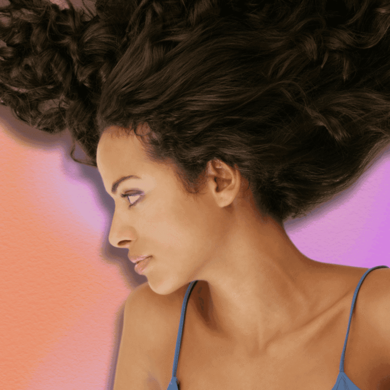 Medium shot of woman with long hair. Background is a orange and pink gradient