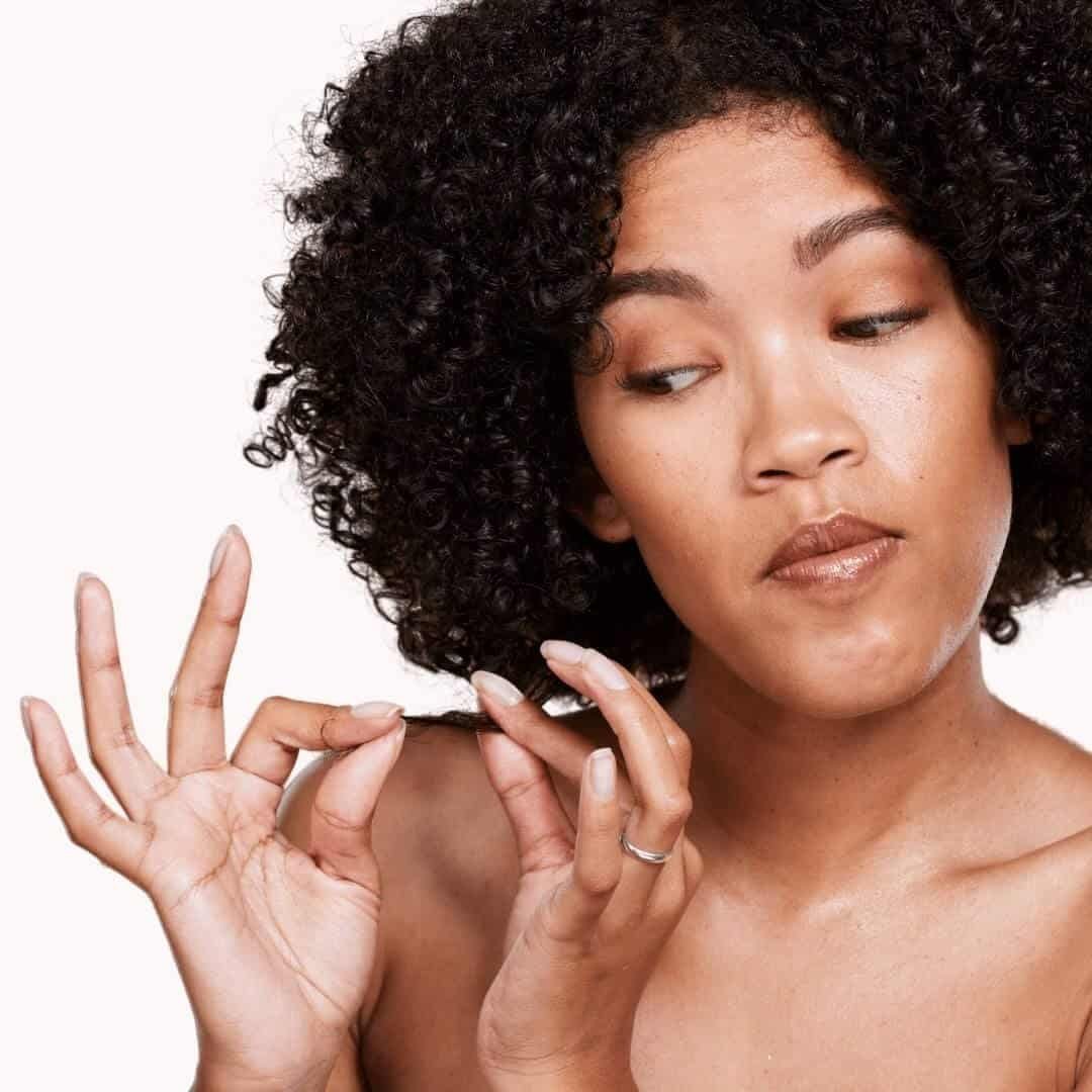 Black woman stretching a strand of her natural hair. Best Deep Conditioners For High Porosity Hair