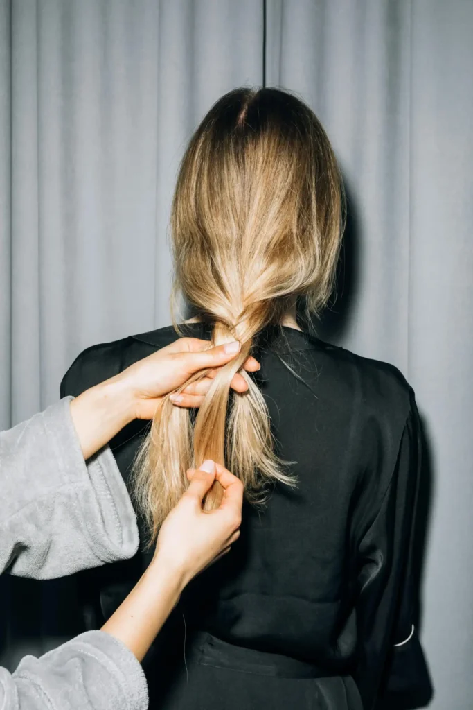backview of woman plaiting someone's blonde hair.
