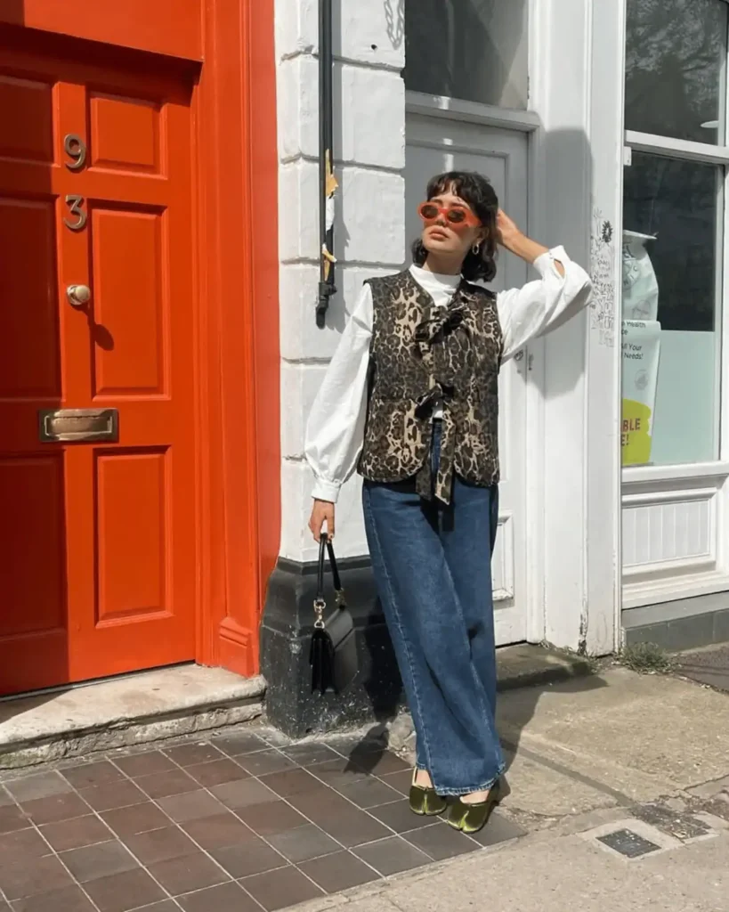 trendy woman wearing a leopard rpint wasitcoat, orange sunglasses, jeans and velvet green tabi shoes