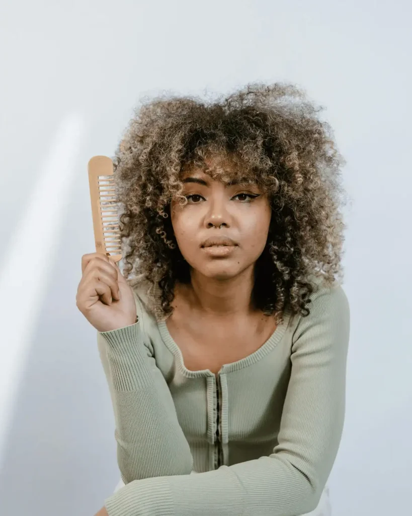 woman with blonde highlight in her afro holding a wooden comb