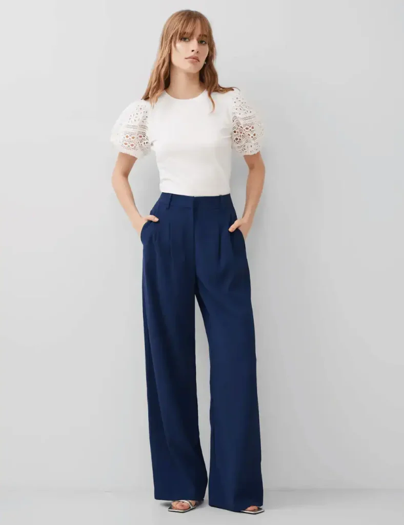model wearing a white top with lace sleeves and navy blue loose-fitting trousers