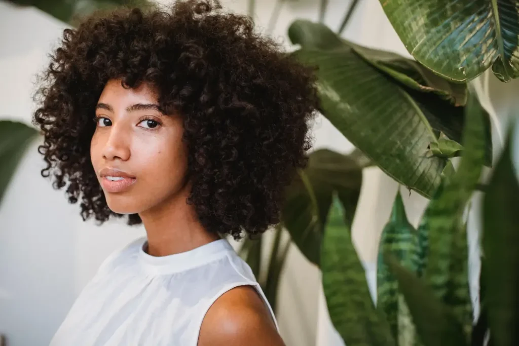 Beautiful portrait of a young woman with natural curly hair in a serene indoor setting with plants. Is Coconut Oil Good for Low Porosity Hair