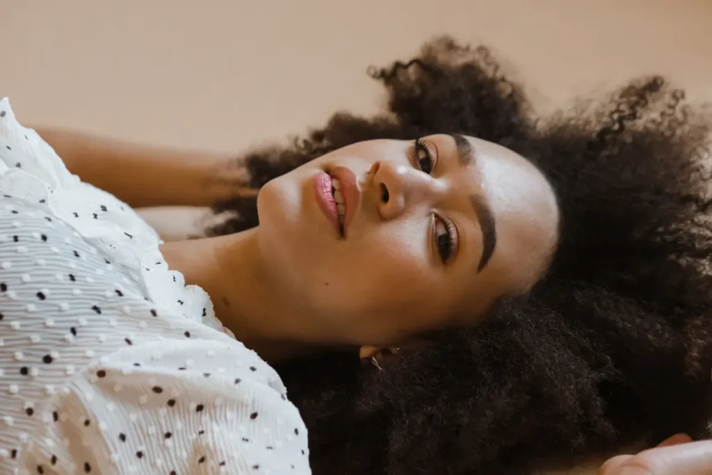 Elegant portrait of a woman with natural curly hair, lying down in a polka dot dress. Is Coconut Oil Good for Low Porosity Hair