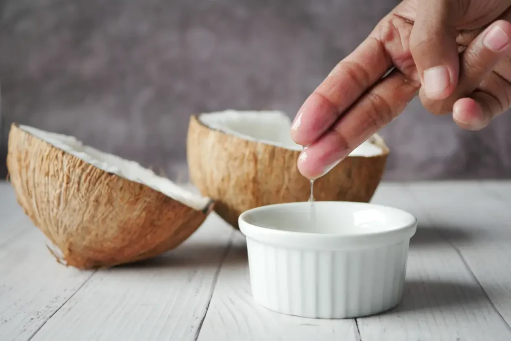 Hand extracting coconut oil into a bowl, ideal for natural skincare routines. Is Coconut Oil Good for Low Porosity Hair
