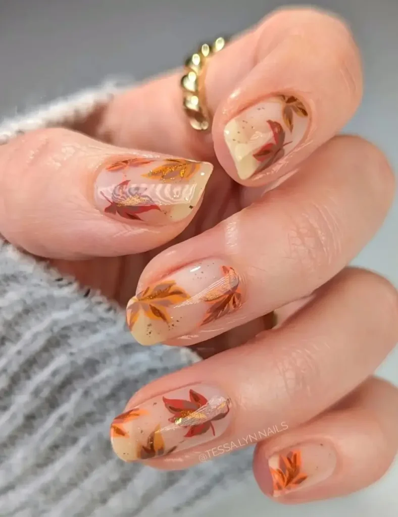 Nude nail set with hand-painted autumn leaf art in orange, red, and gold tones.
