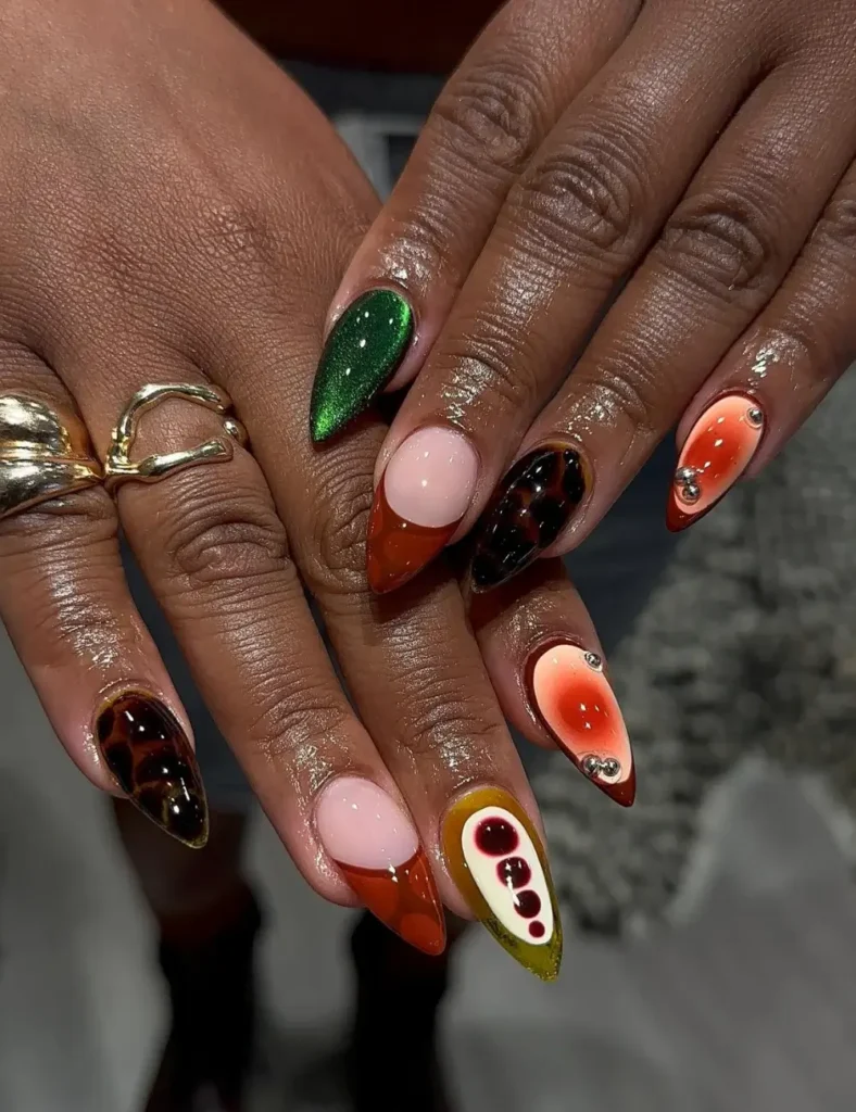 Mixed-design stiletto nails in emerald, tortoiseshell, orange, and cream with pearl embellishments.