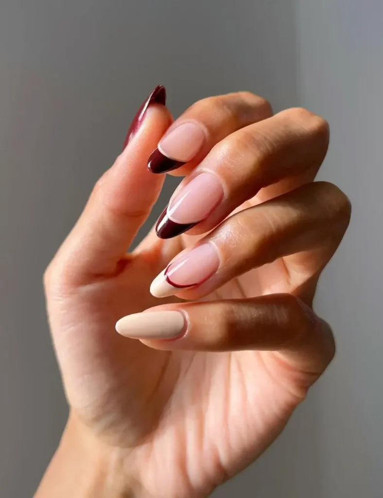 Almond nails with sheer nude base and deep burgundy French tip design.