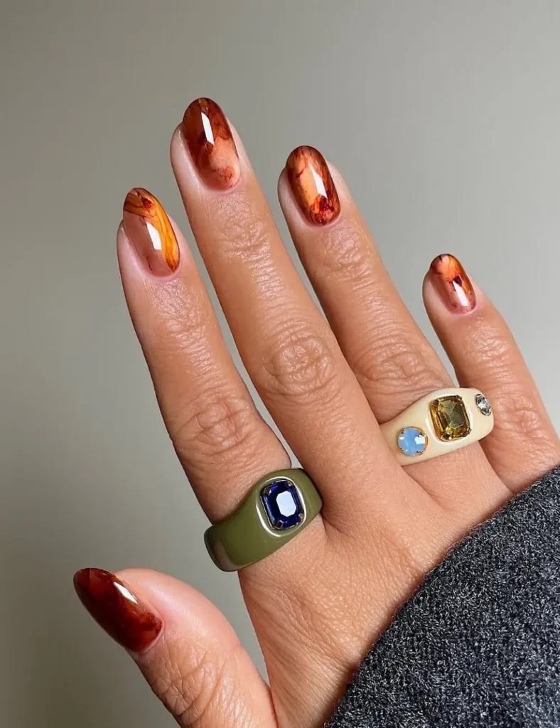 Short round nails with amber and rust marbled nail art design.