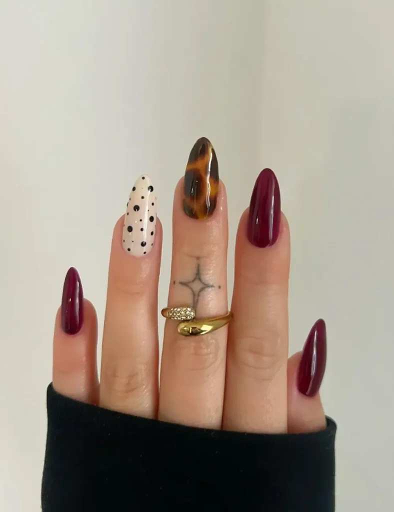 Berry-colored nails with one polka dot accent nail and one tortoiseshell accent nail.