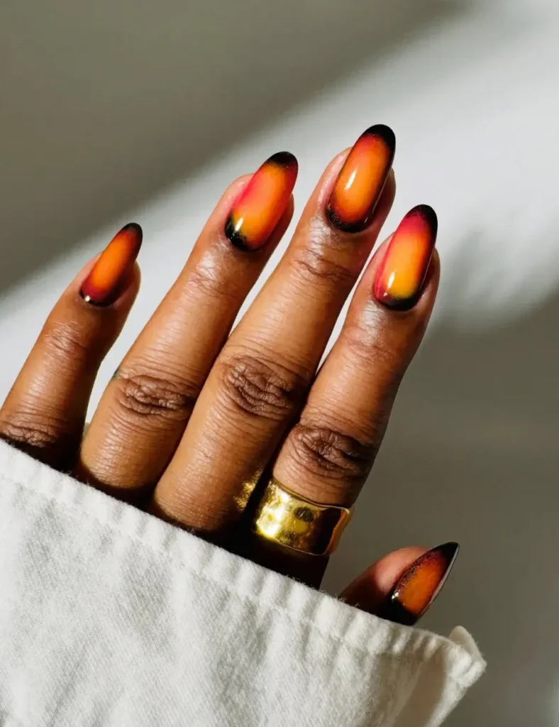 Almond-shaped nails with a black-to-orange-to-yellow sunset ombrรฉ design.