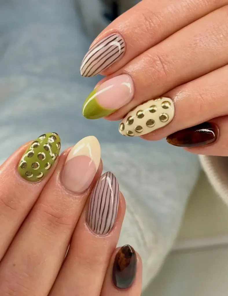 Mismatched manicure featuring olive green, cream, and brown nails with striped and gold polka dot designs.