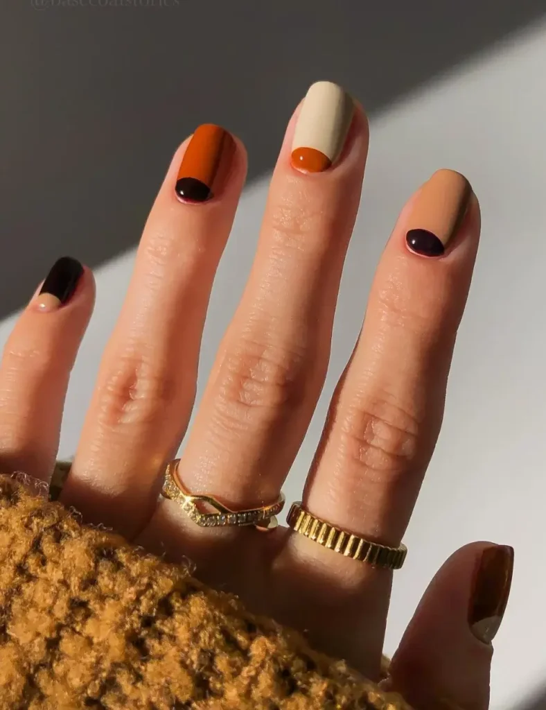Color block manicure with burnt orange, black, and cream half-moon nail designs.