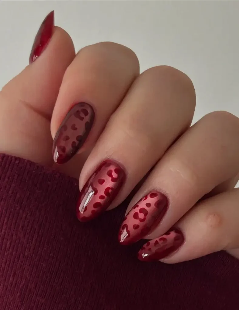 Almond nails with deep red base and tonal red leopard print design.