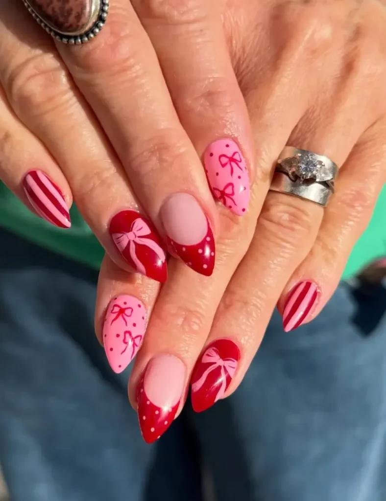 Almond nails in a pink and red mix with bow designs, red stripes, and red French tips with white dots