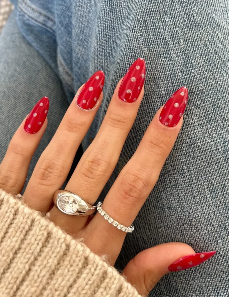 Almond nails painted deep red with small, soft white polka dots