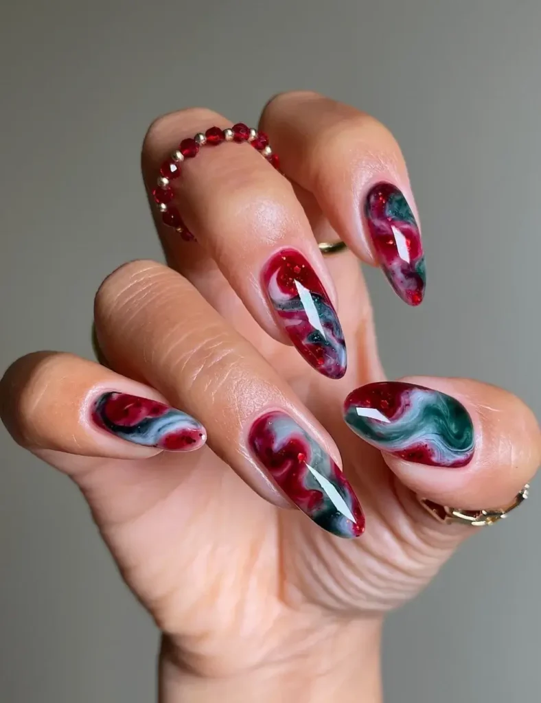 Almond nails with a marbled red, green, and white swirl design and gold foil flecks