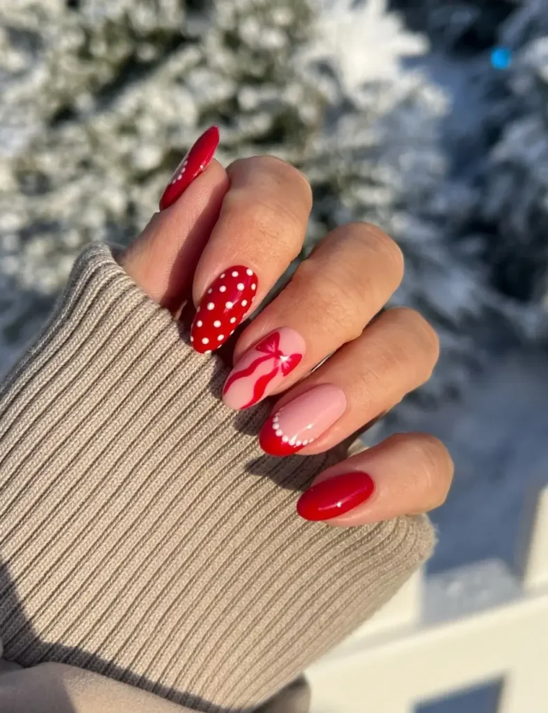 Almond nails with a mix of glossy red, red with white polka dots, pink with a red bow, and a nude nail with a red French tip edged in white dots