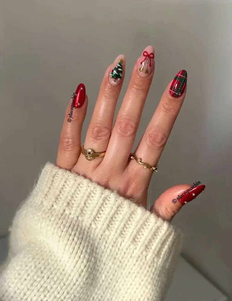 Almond nails with chrome red polish, a nude nail with a Christmas tree, a nude nail with a red bow, and a red tartan accent nail