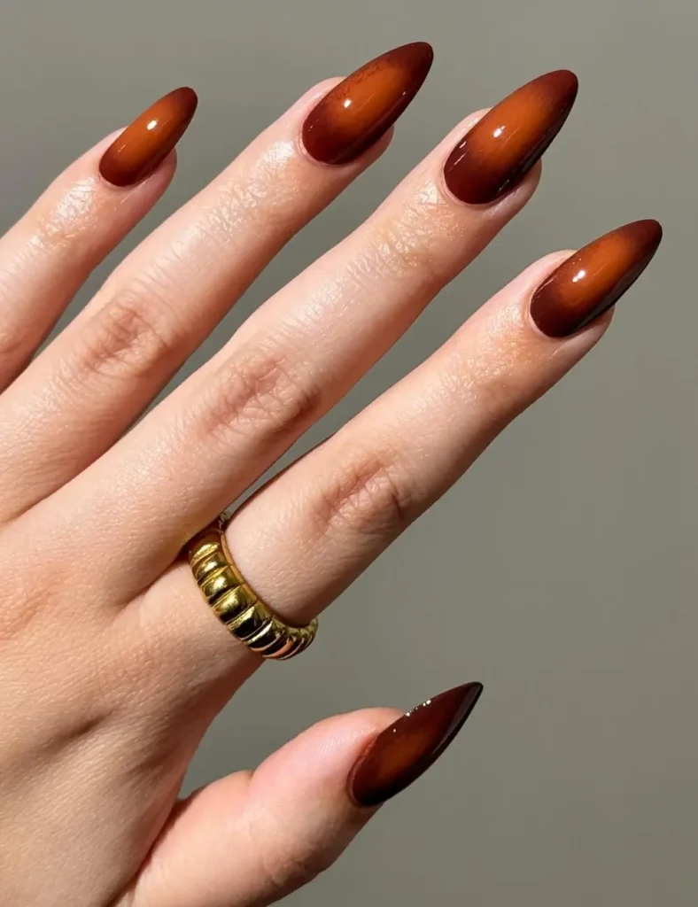 Glossy almond nails with a warm amber glow fading into rich cinnamon brown tips