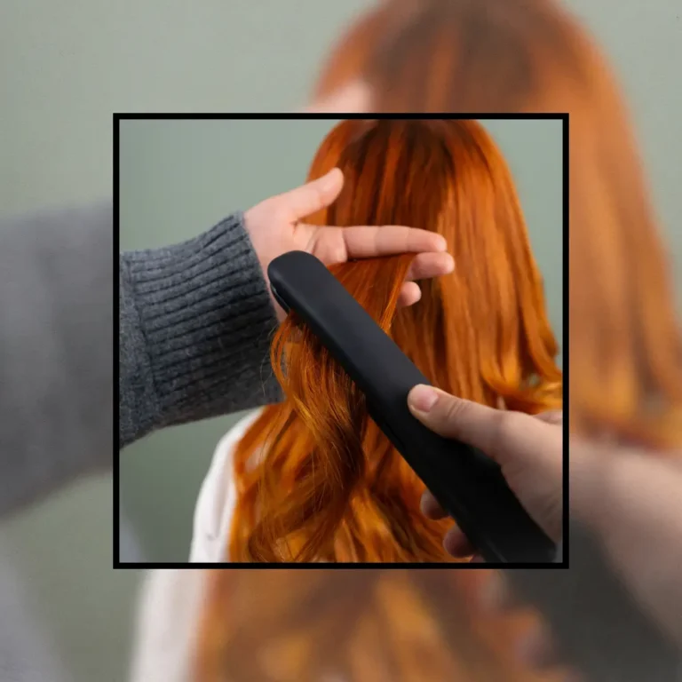 Hands using a black flat iron to straighten a small section of long, wavy copper-red hair, illustrating how to use a hair straightener safely