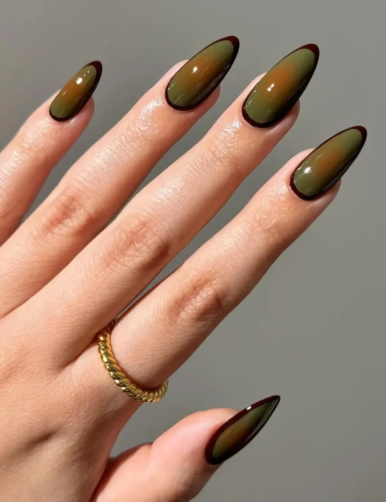 Long almond nails in olive green with a glowing amber center and a dark brown outlined edge