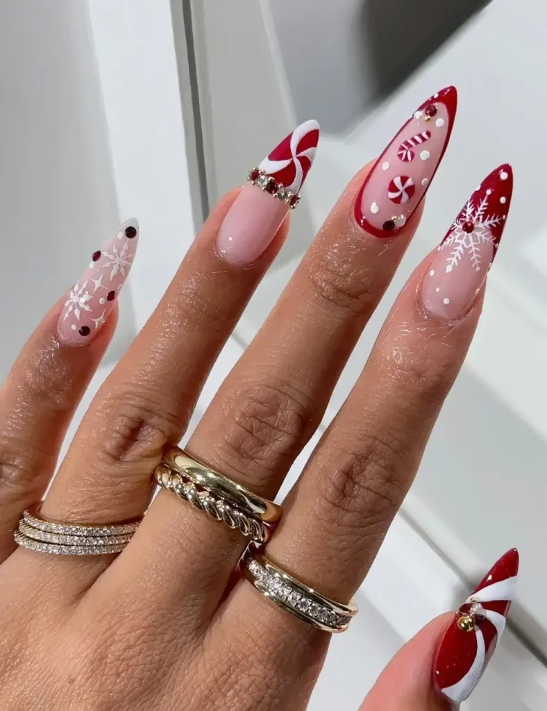 Long almond nails with nude bases, peppermint candy swirls, white snowflakes, and a red French tip with white dots and gems