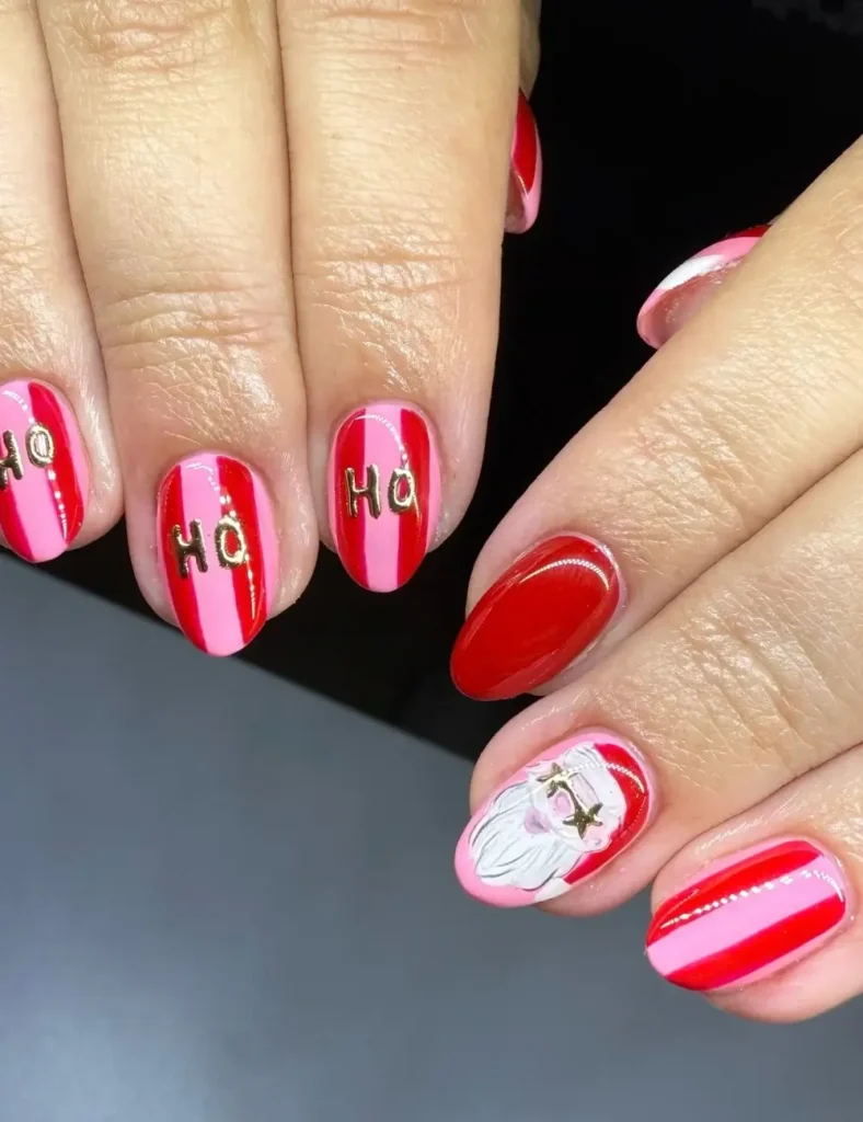 Short nails with pink and red stripes, gold โHOโ lettering, a solid red nail, and a Santa face accent nail