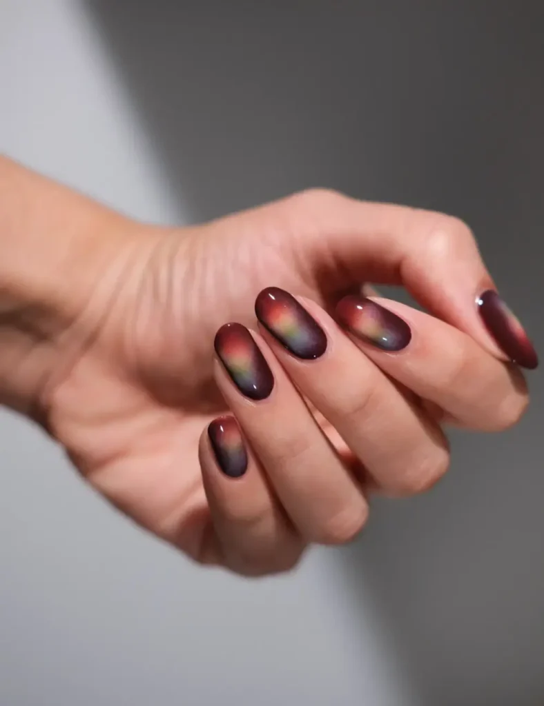 Short rounded nails with a dark base and soft multicolor aura glows in pink, green, and amber