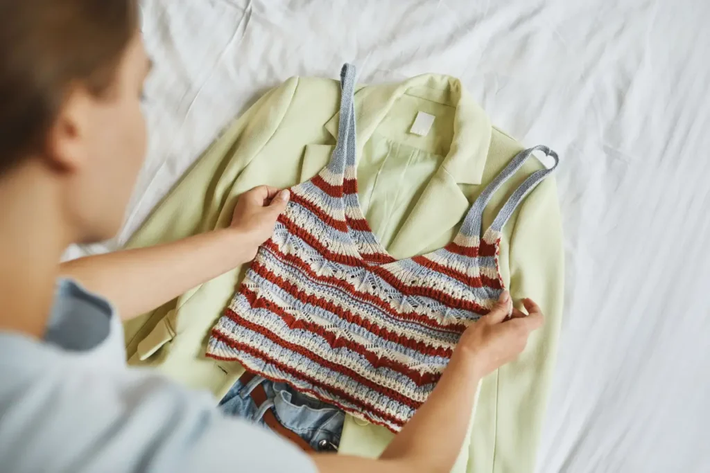Woman arranging a stylish blazer and knitted top outfit on a bed