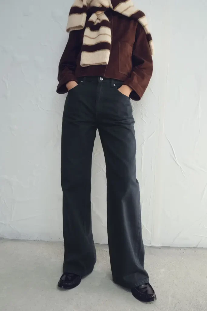 Woman wearing Mango mid-rise straight-leg jeans in a dark charcoal wash, styled with a brown jacket and a striped sweater