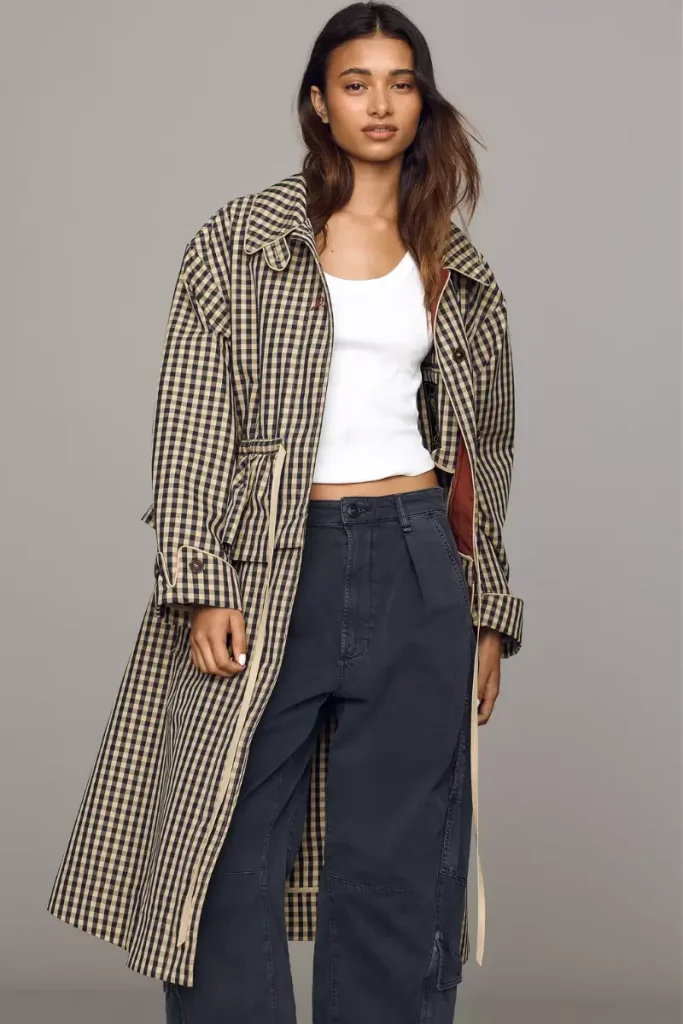 Woman wearing a Damson Madder navy longline trench coat with a classic collar, button front, and peplum waist