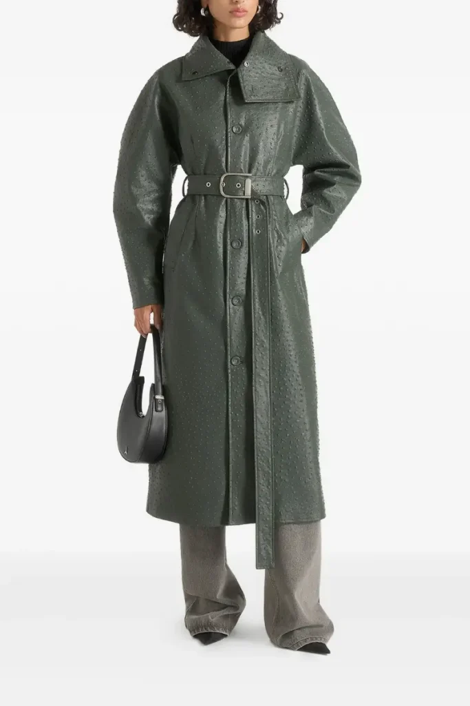 Woman wearing a Maniรจre De Voir deep green faux ostrich-effect trench coat with balloon sleeves, an hourglass belted waist, and a funnel neck