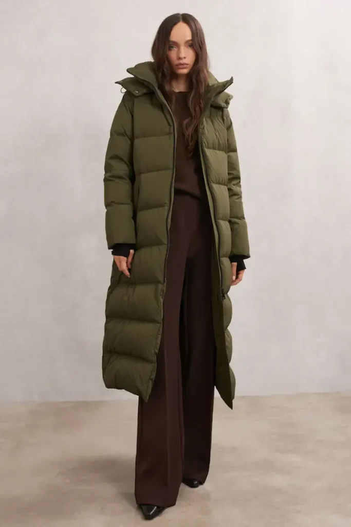 Woman wearing a Reiss Colette khaki longline quilted puffer coat with a hood and buckled waist belt