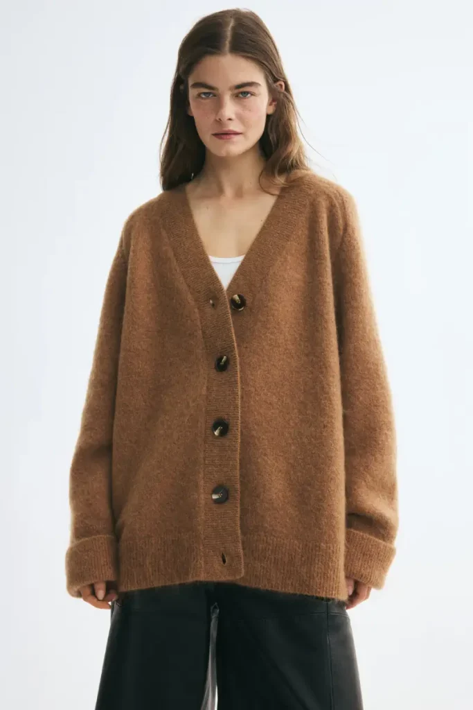 Woman wearing an H&M oversized dark beige mohair-blend cardigan with a V-neck and tortoiseshell buttons, styled over a white top with black leather pants