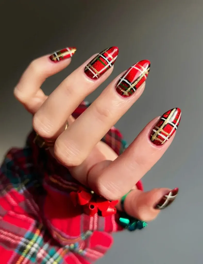 Almond nails painted in red tartan plaid with gold and white lines, held against a red plaid sleeve